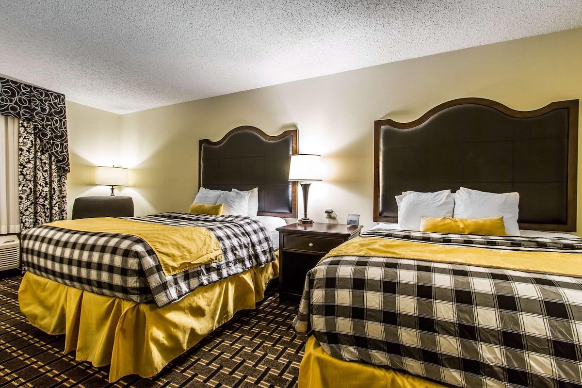 A hotel room with two beds, a nightstand, a lamp, and a decorative wall panel.