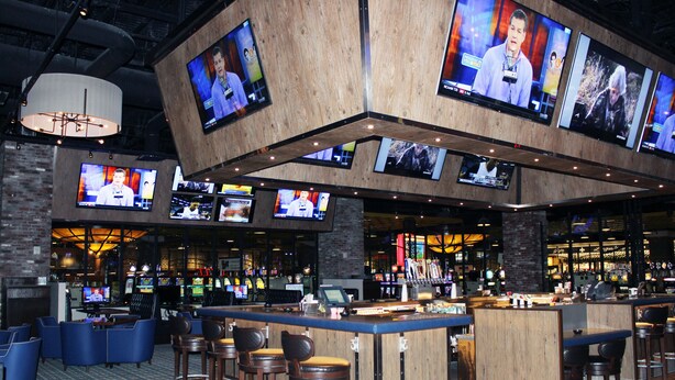 A bar area with multiple TVs mounted on the ceiling, a bar counter, and several seating areas with stools.