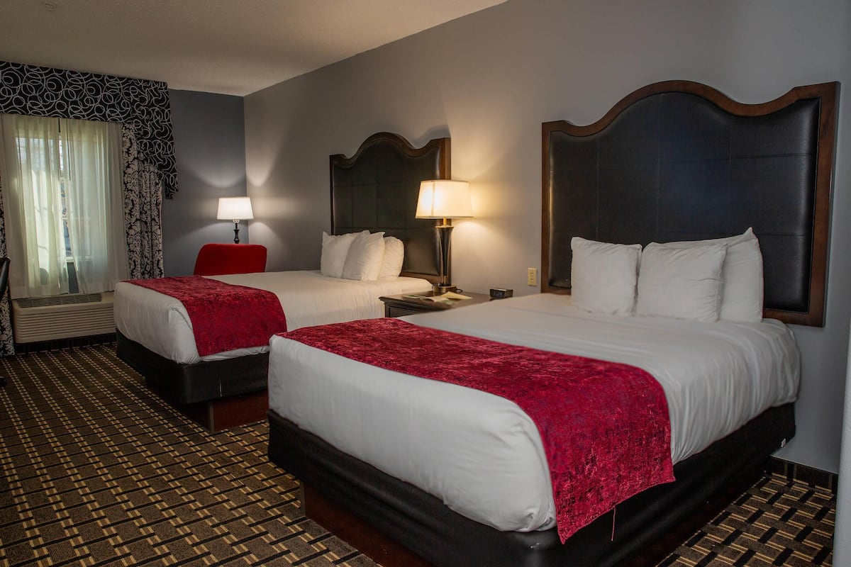 A hotel room with two beds, each with a red blanket, a nightstand with a lamp, and a large mirror on the wall.