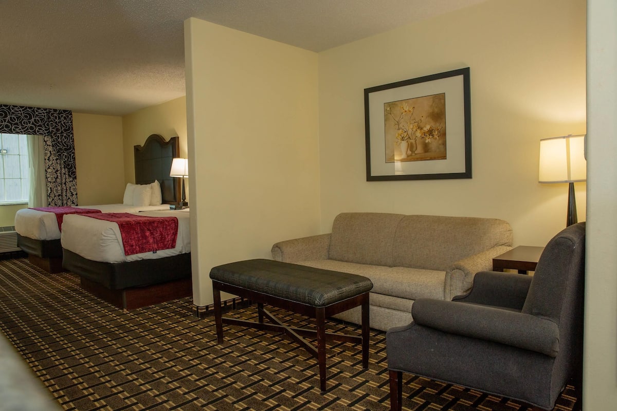 A hotel room with two beds, a sofa, a chair, a small table, and a framed picture on the wall.