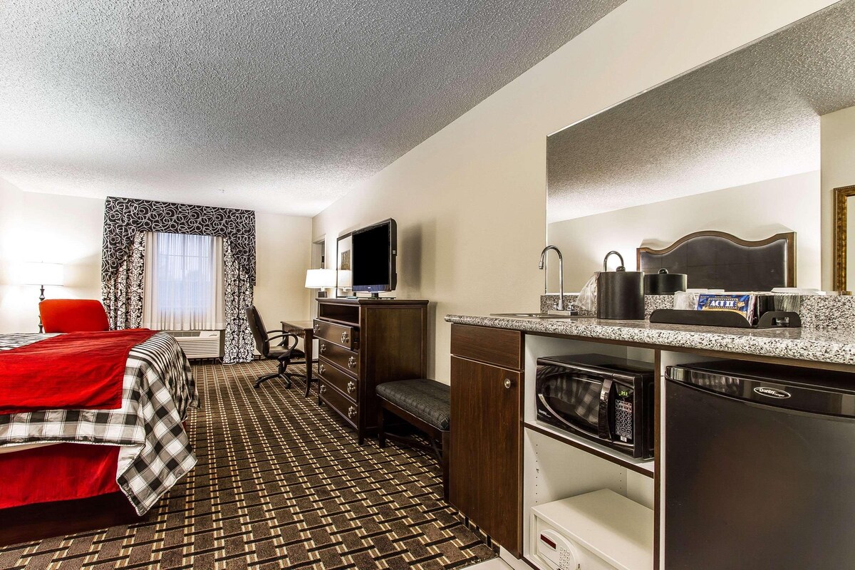 A hotel room with a bed, a desk, a television, a microwave, a refrigerator, and a bathroom.