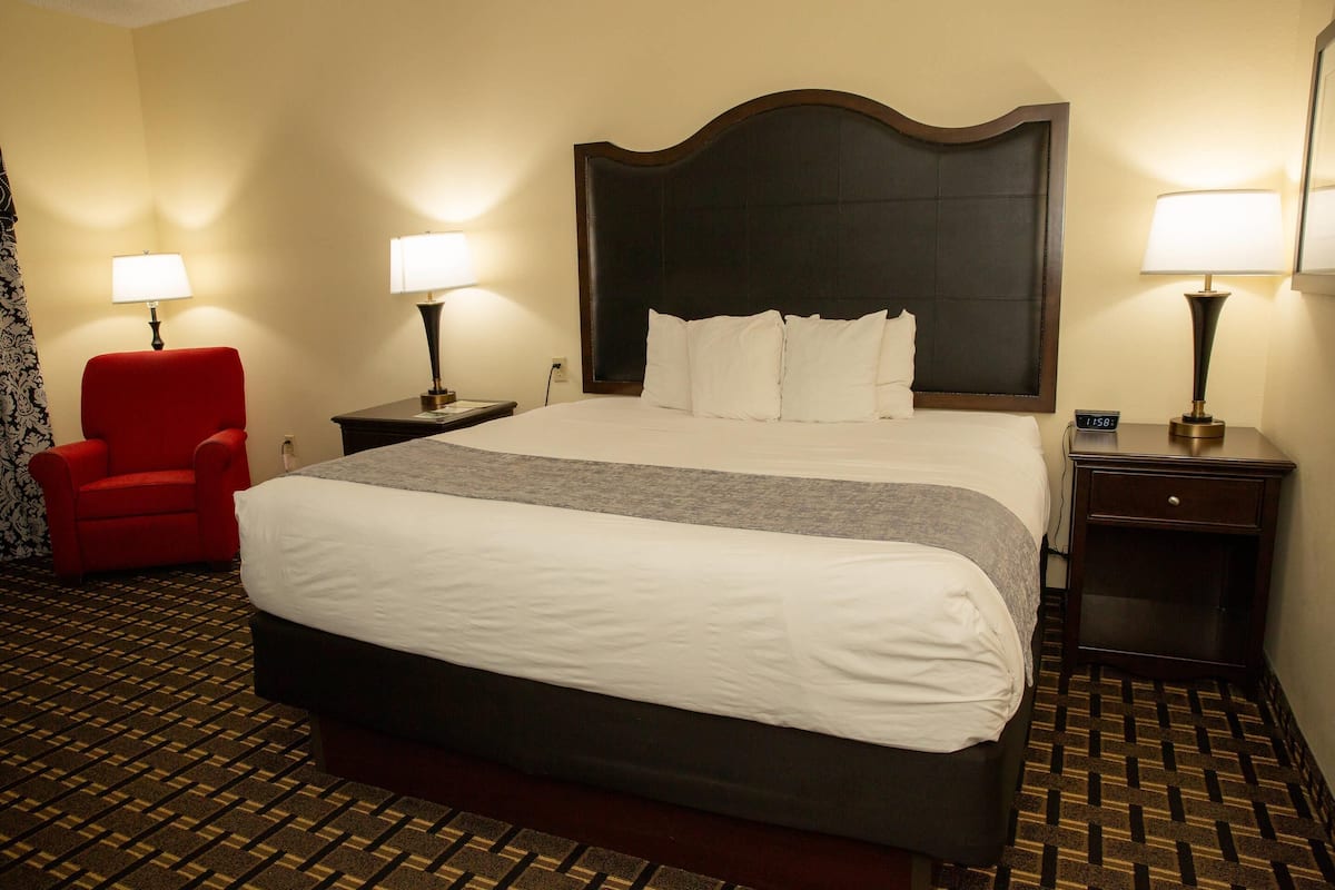 A hotel room with a large bed, two bedside tables with lamps, a red chair, and a patterned carpet.