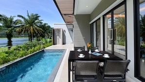 A modern outdoor dining area with a pool, overlooking a scenic view of palm trees and a body of water. - Tinidee Golf Resort Phuket (Kathu)