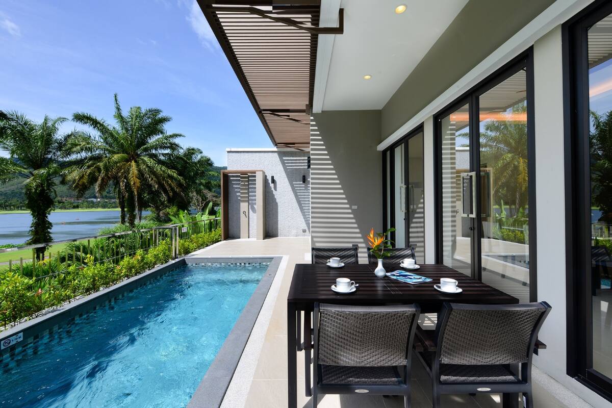 A modern outdoor dining area with a pool, overlooking a scenic view of palm trees and a body of water.
