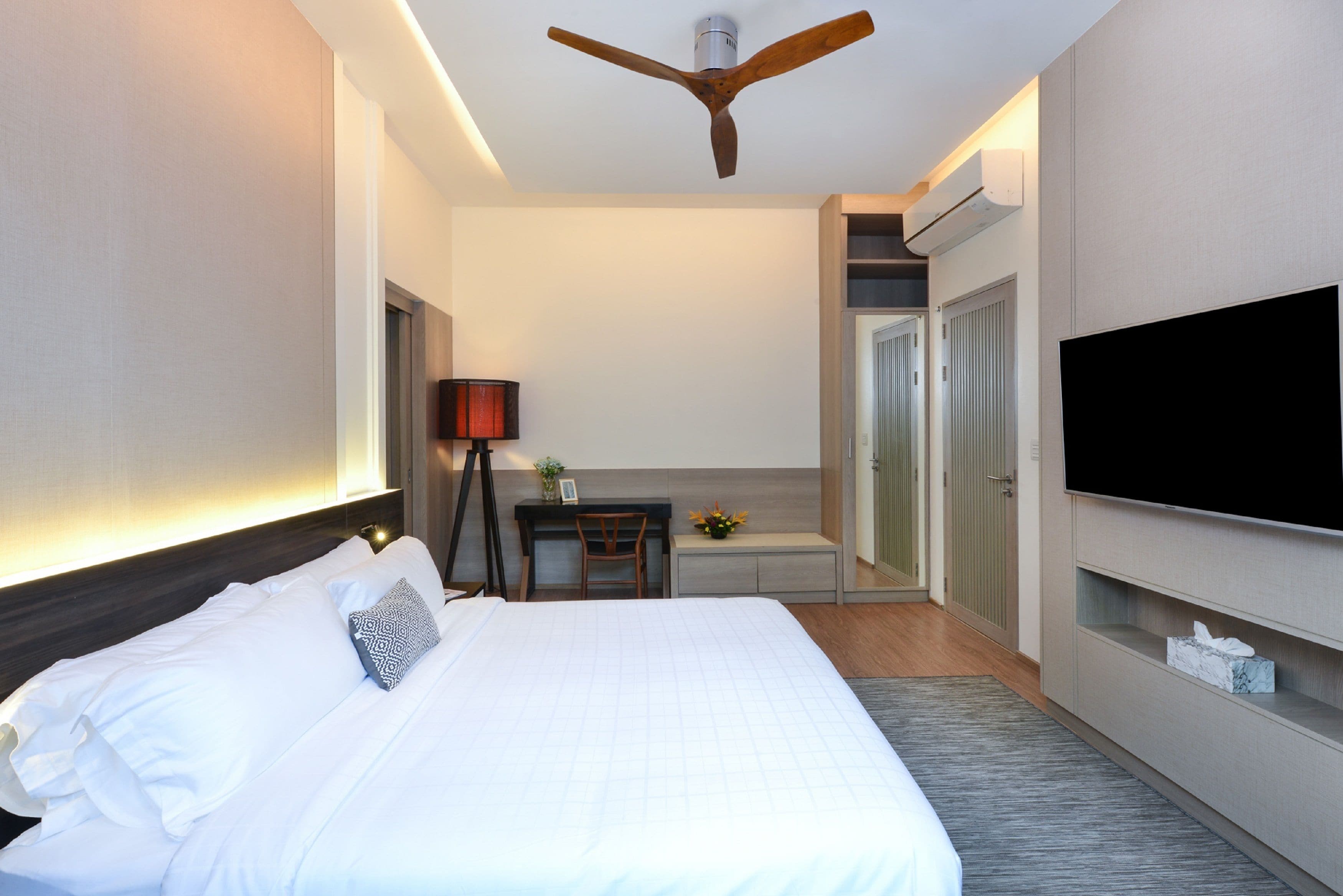 A modern hotel room with a large bed, a desk, a ceiling fan, a flat-screen TV, and a walk-in closet.