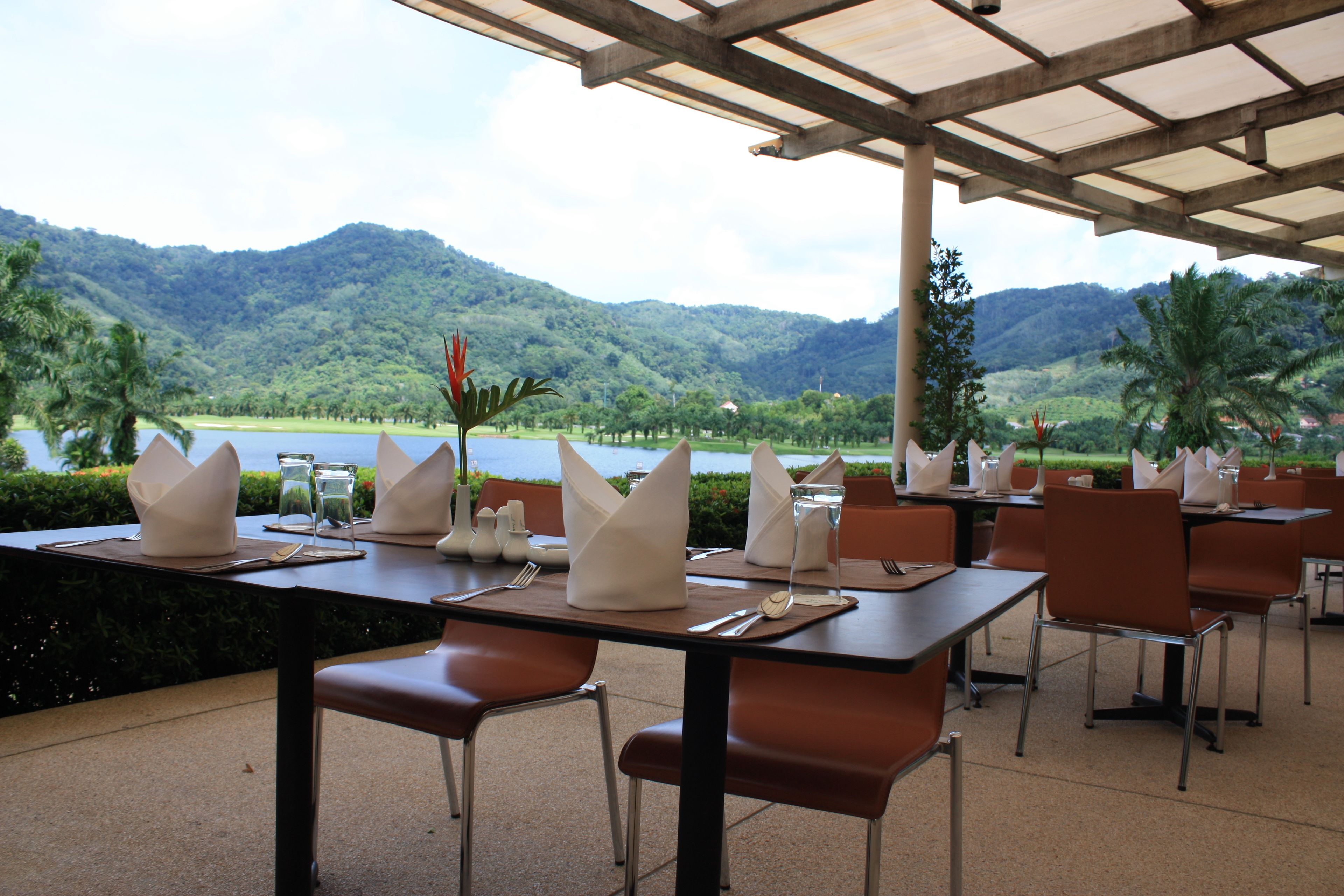 A restaurant with tables set for dining, overlooking a lake and mountains.
