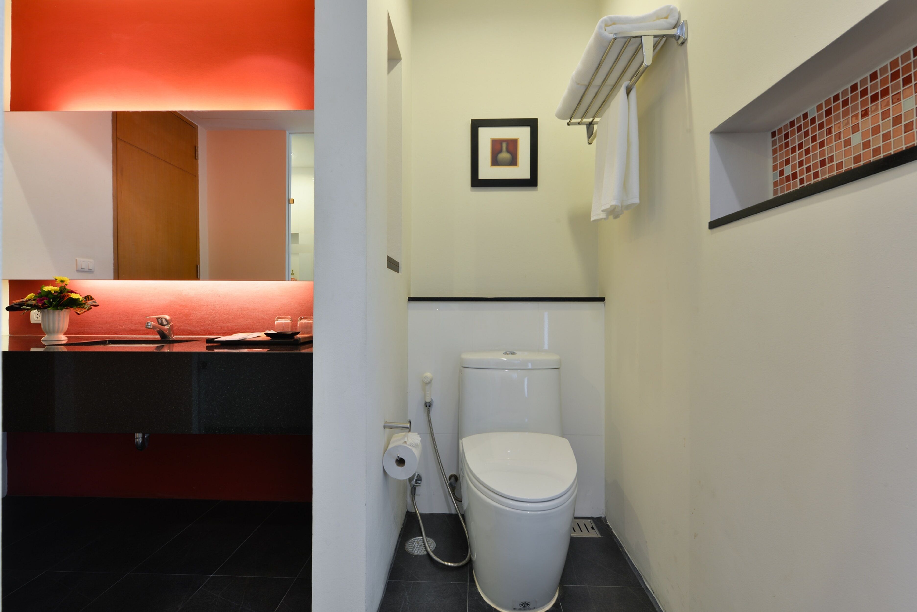 A bathroom with a toilet, a sink with a red countertop, a towel rack, and a small framed picture on the wall.