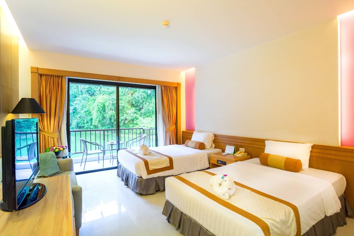 A hotel room with two beds, a TV, a balcony, and a view of greenery.