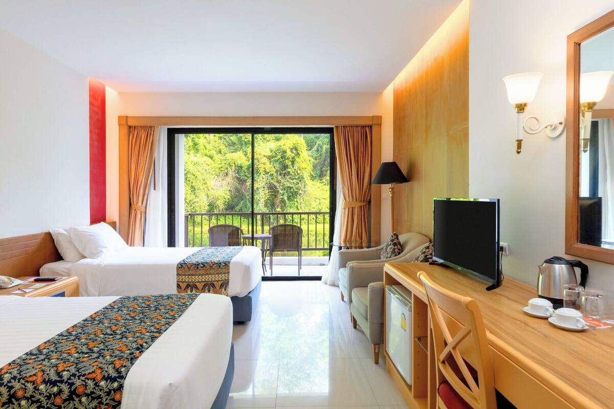 A hotel room with two beds, a desk with a TV, a chair, a sofa, and a balcony with curtains.