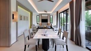 A modern dining area with a long table, chairs, ceiling fans, and large windows with curtains. - Tinidee Golf Resort Phuket (Kathu)