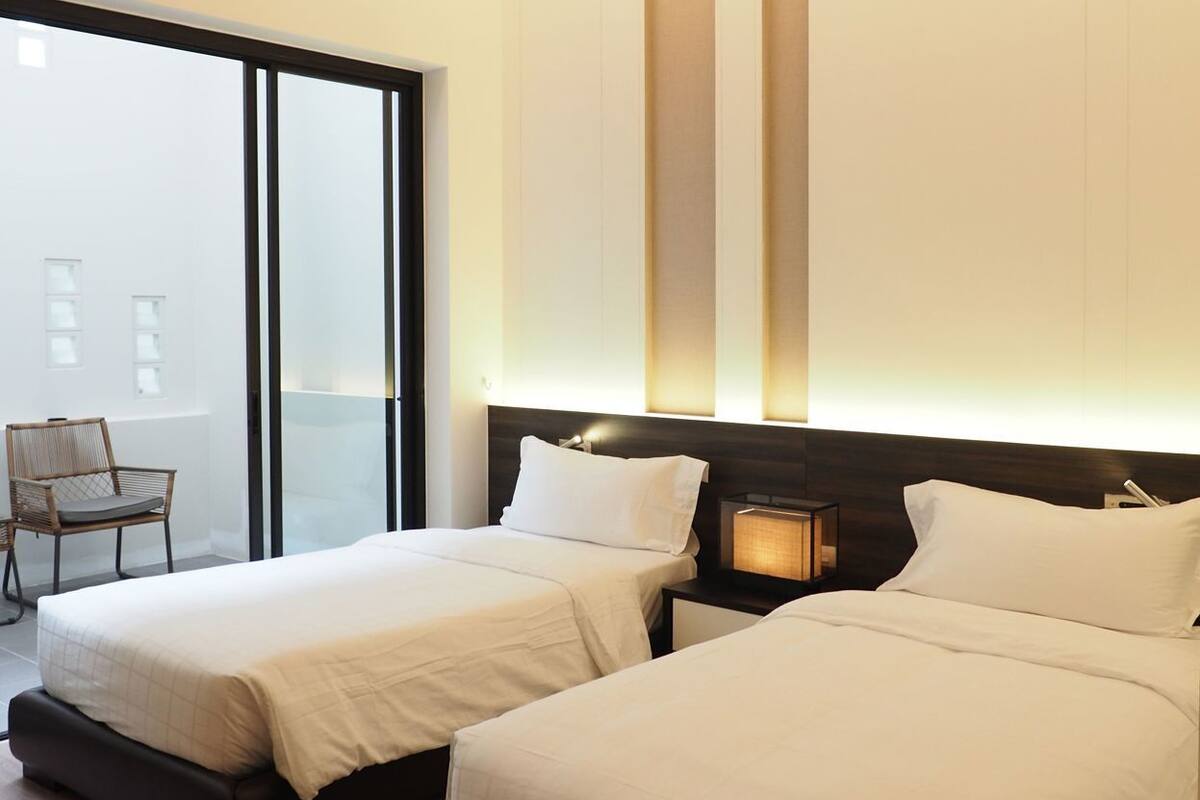 A hotel room with two beds, a chair, a ceiling fan, and a view through a large window.