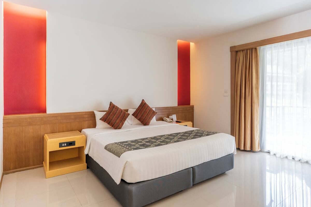 A modern hotel room with a large bed, bedside tables, a nightstand, and a large window with curtains.