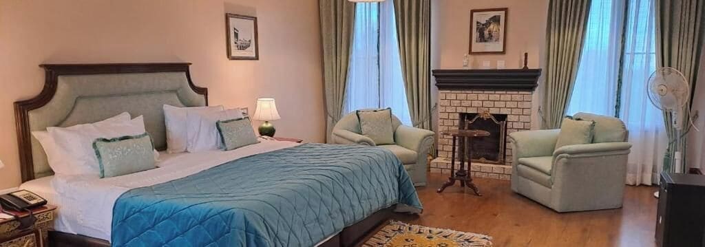 Una habitación de hotel con una cama grande, dos sillones, una chimenea y una mesita.