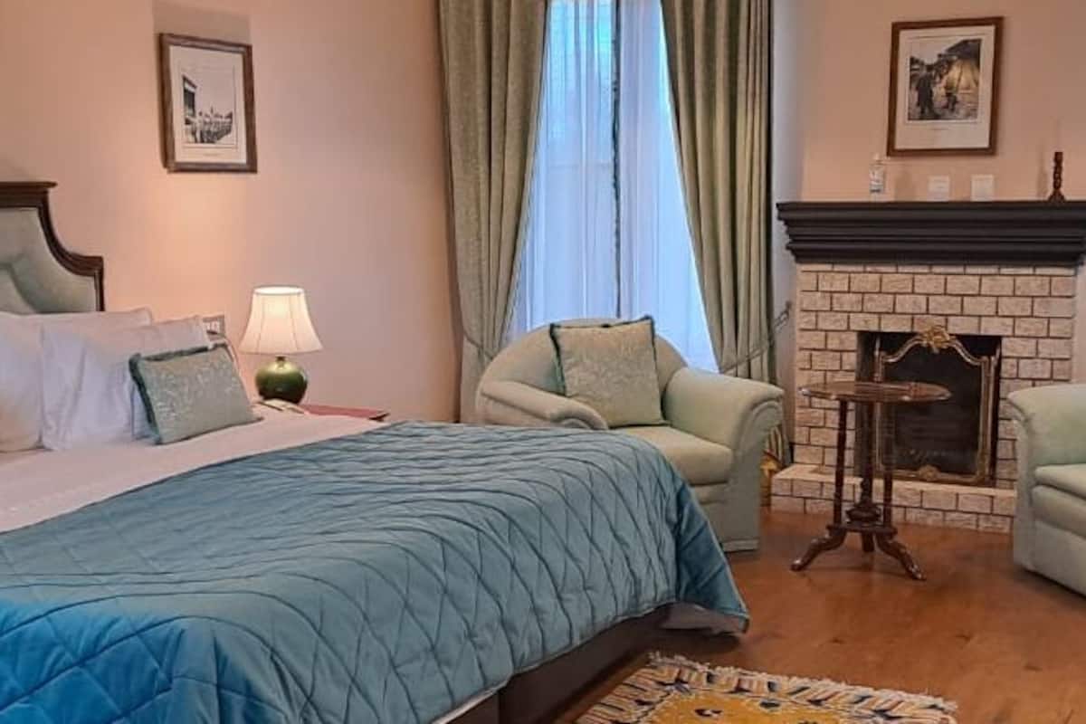 Quarto de hotel com uma cama grande, duas poltronas, lareira e uma pequena mesa.