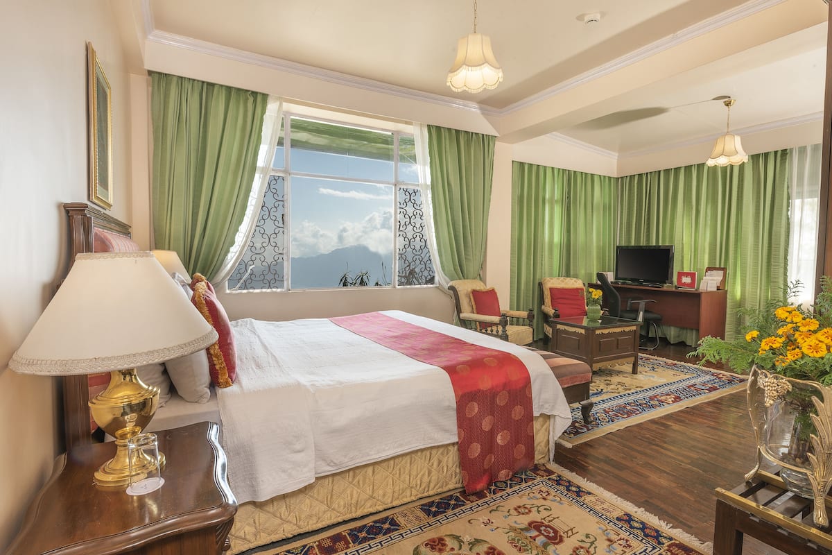 Quarto de hotel com uma cama grande, uma escrivaninha, televisão e vista para as montanhas.