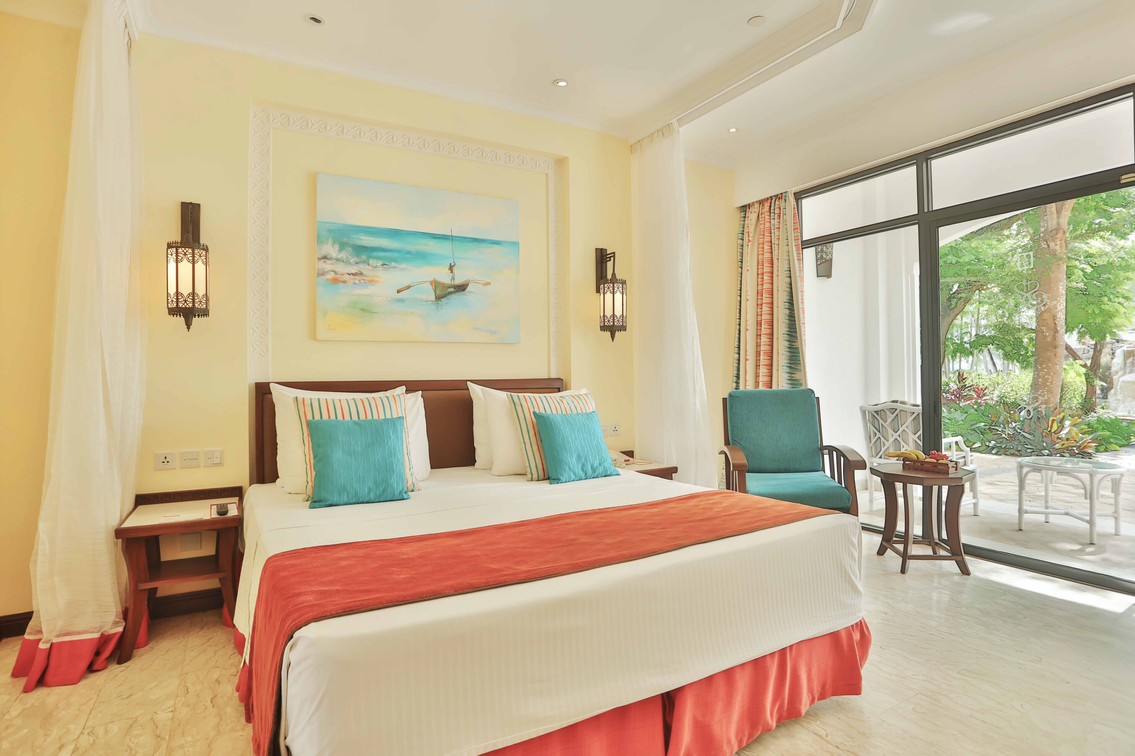 A hotel room with a large bed, two bedside tables, a chair, a small table, and a view of the outdoors.