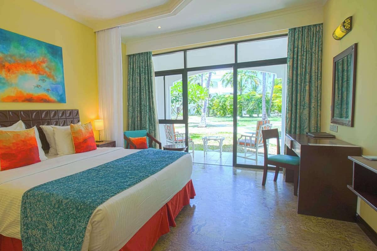 A hotel room with a large bed, a desk, and a view of a garden through the sliding glass door.
