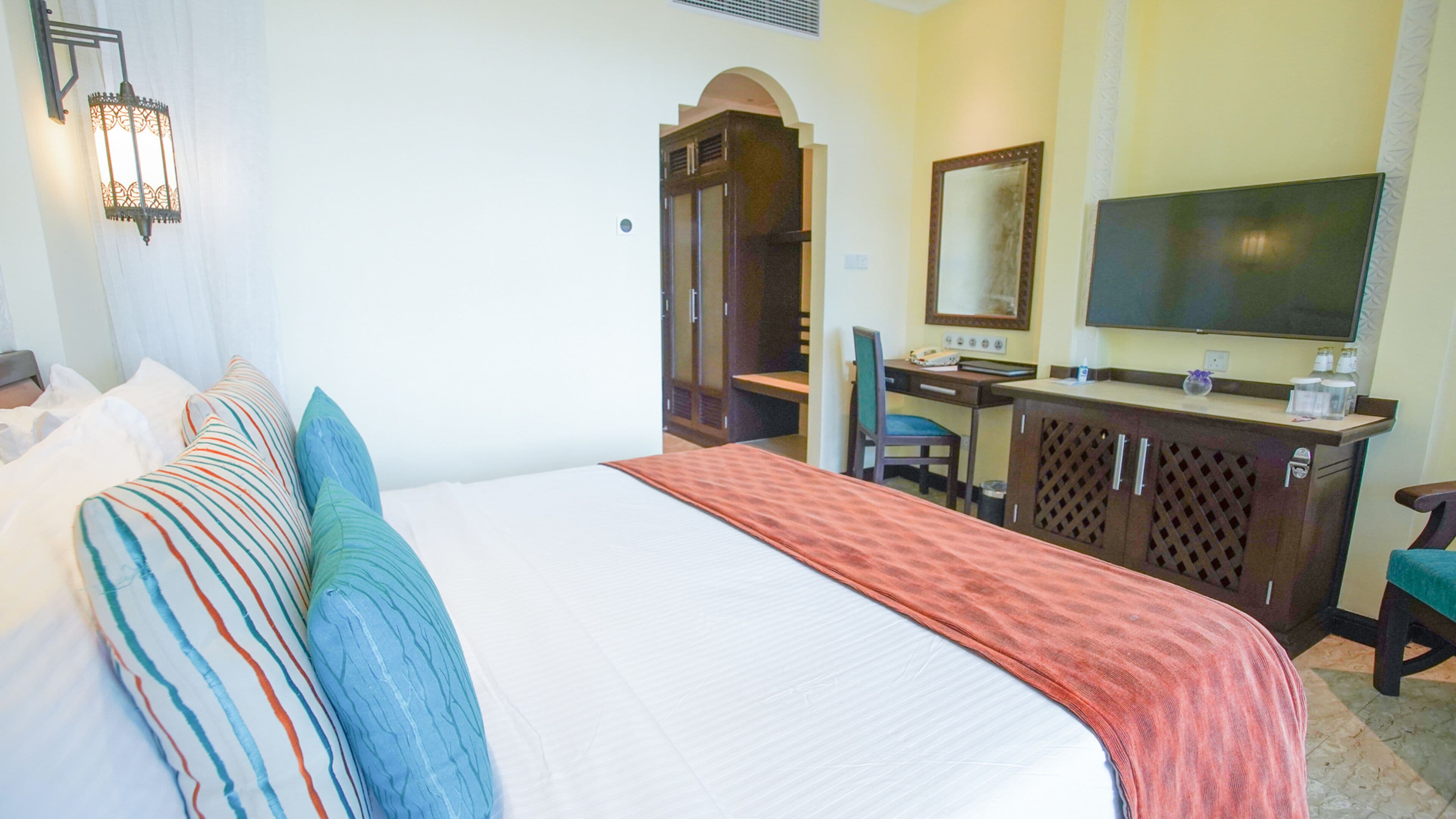 Une chambre d’hôtel avec un grand lit, un bureau, une chaise, un miroir et un téléviseur.