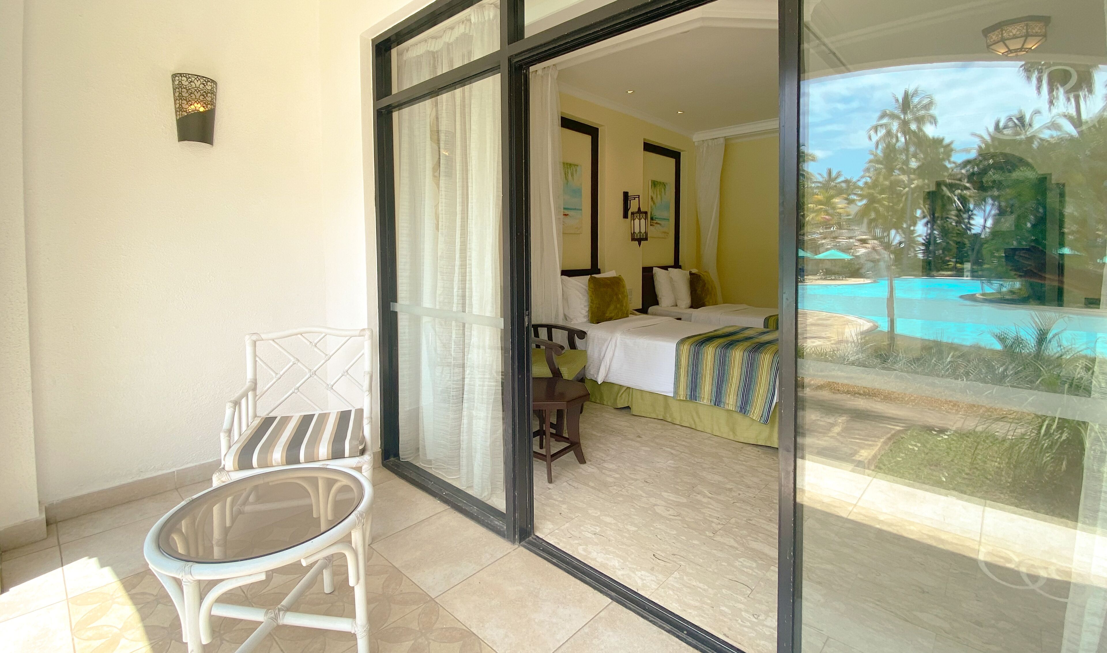 A balcony with a glass door leading to a bedroom with a bed, a chair, and a small table.