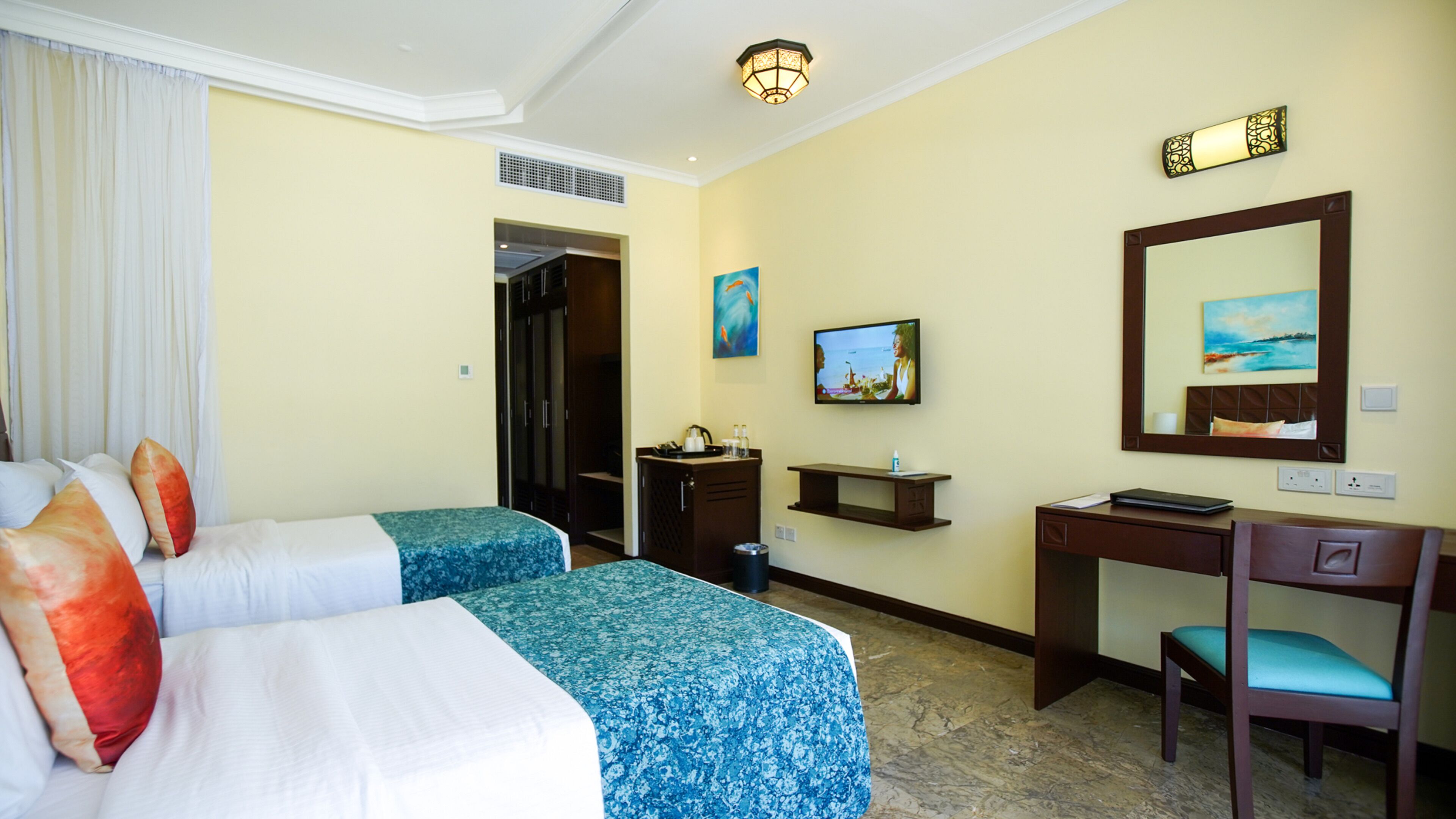 A hotel room with two beds, a desk, a chair, a TV, and a painting on the wall.