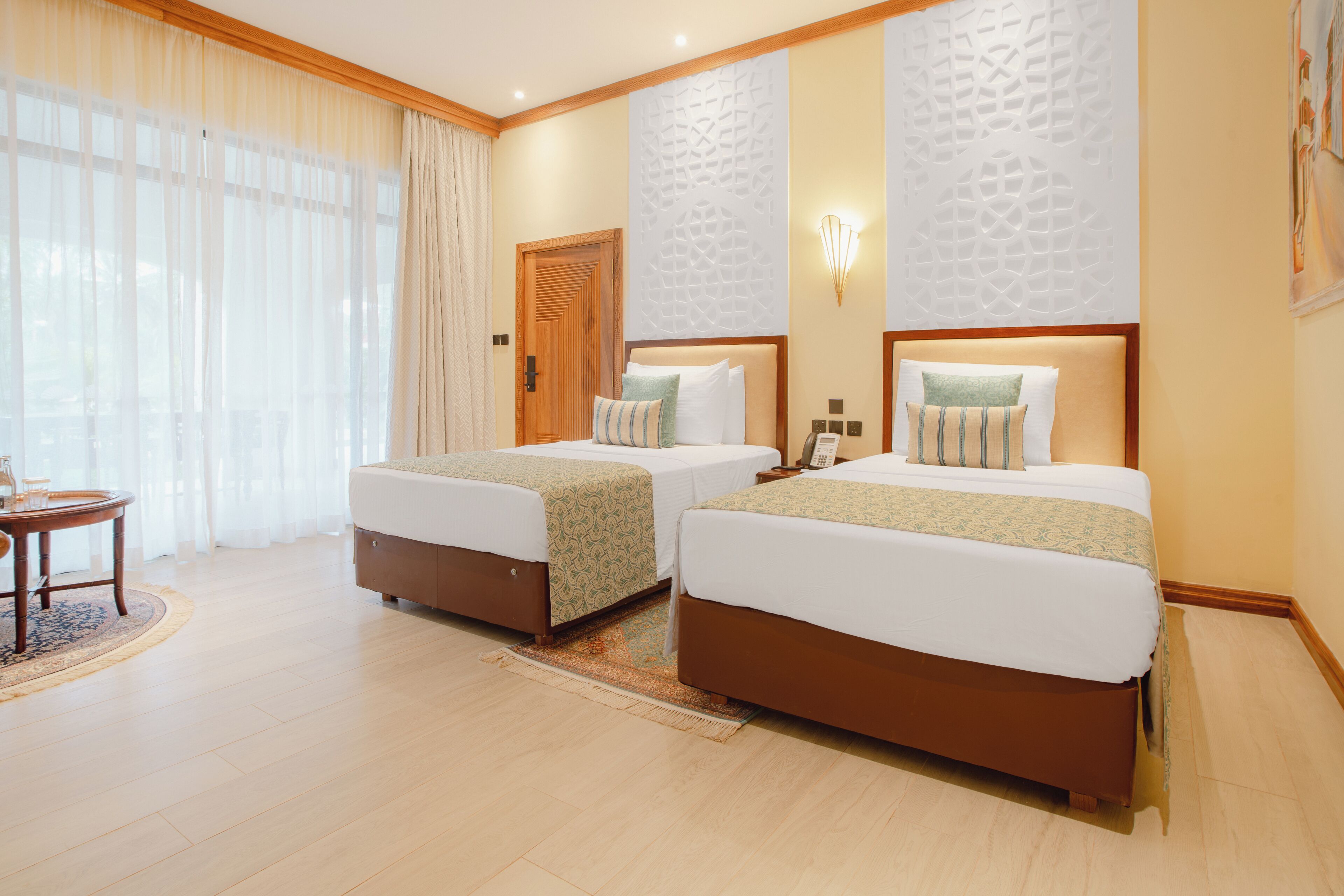 Habitación de hotel con dos camas, una puerta de madera, un teléfono en la pared y una pequeña mesa con una silla.