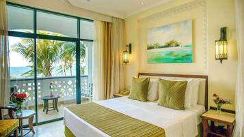 A hotel room with a large bed, a balcony with a view of the sea, and a painting on the wall.