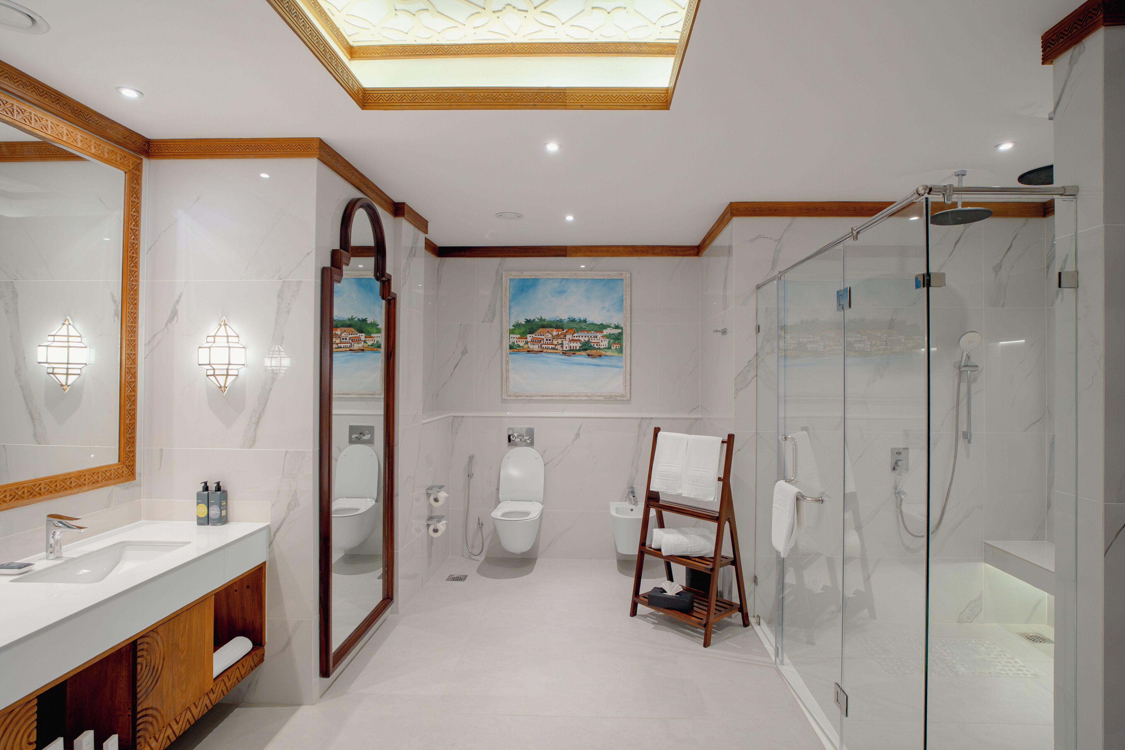 Un baño moderno con ducha de vidrio, un espejo grande y un cuadro de una escena costera.