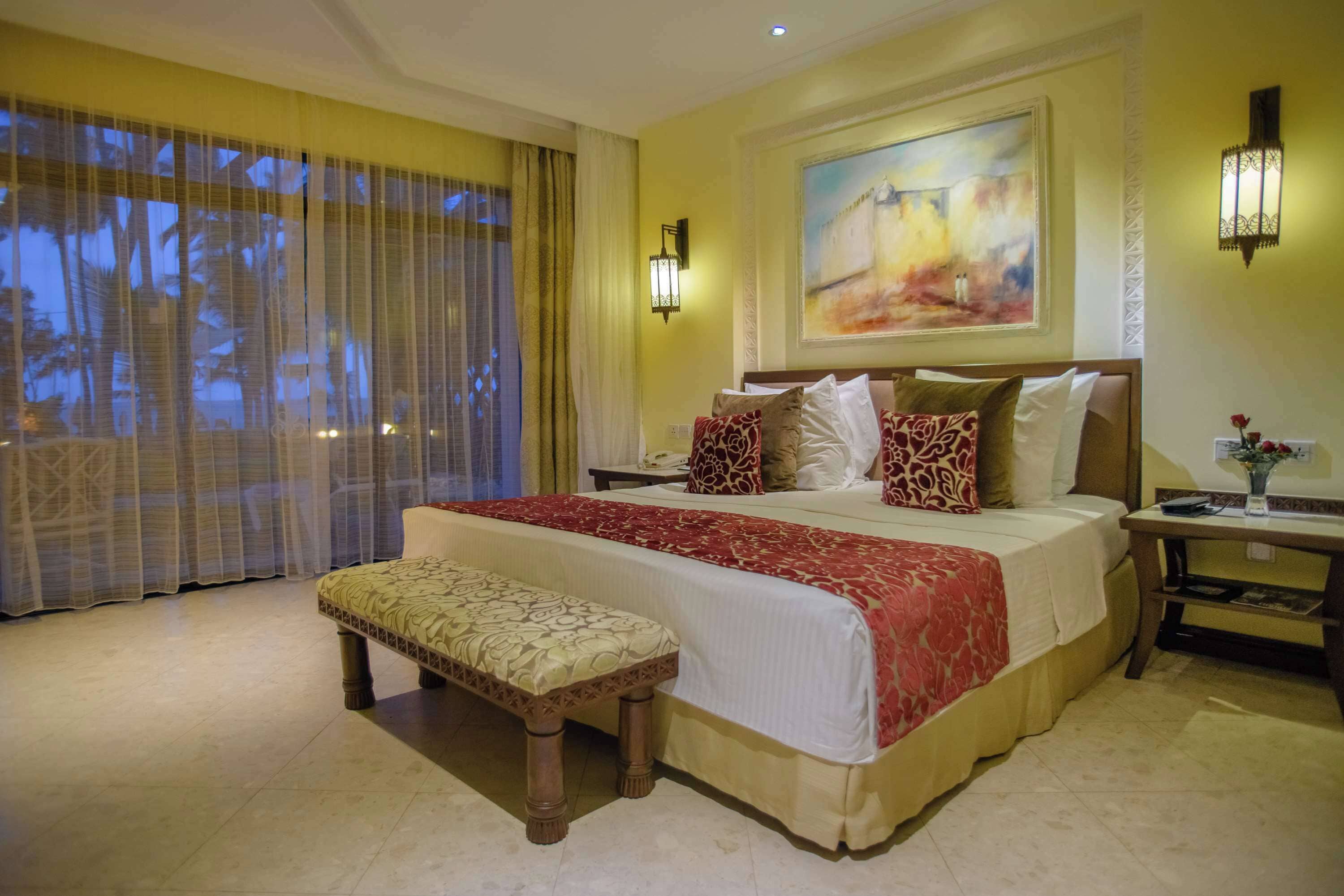 Una habitación de hotel con una cama grande, un banco, una mesita de noche y un cuadro en la pared.