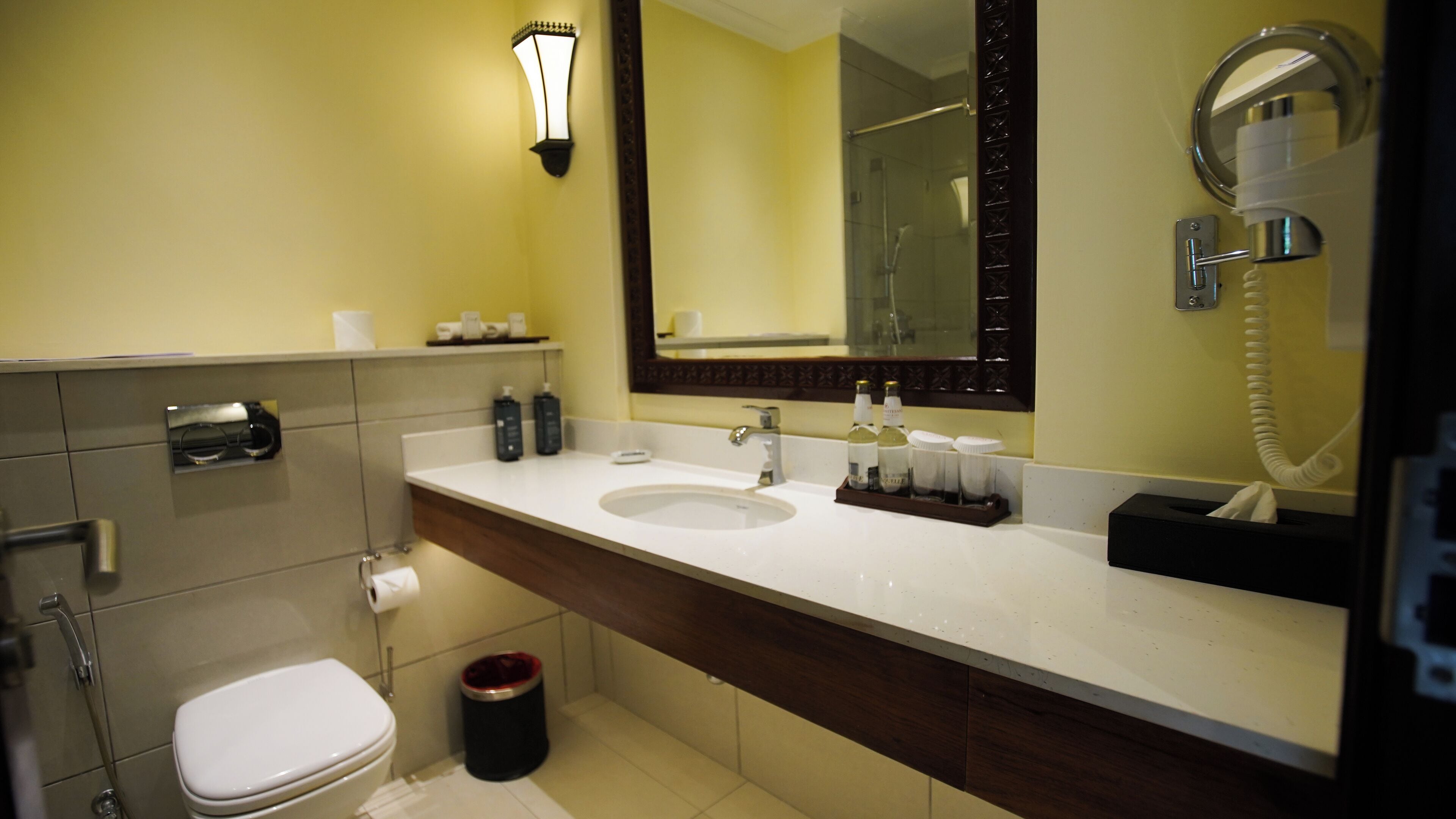 A bathroom with a white sink, a mirror, a toilet, and a trash can.