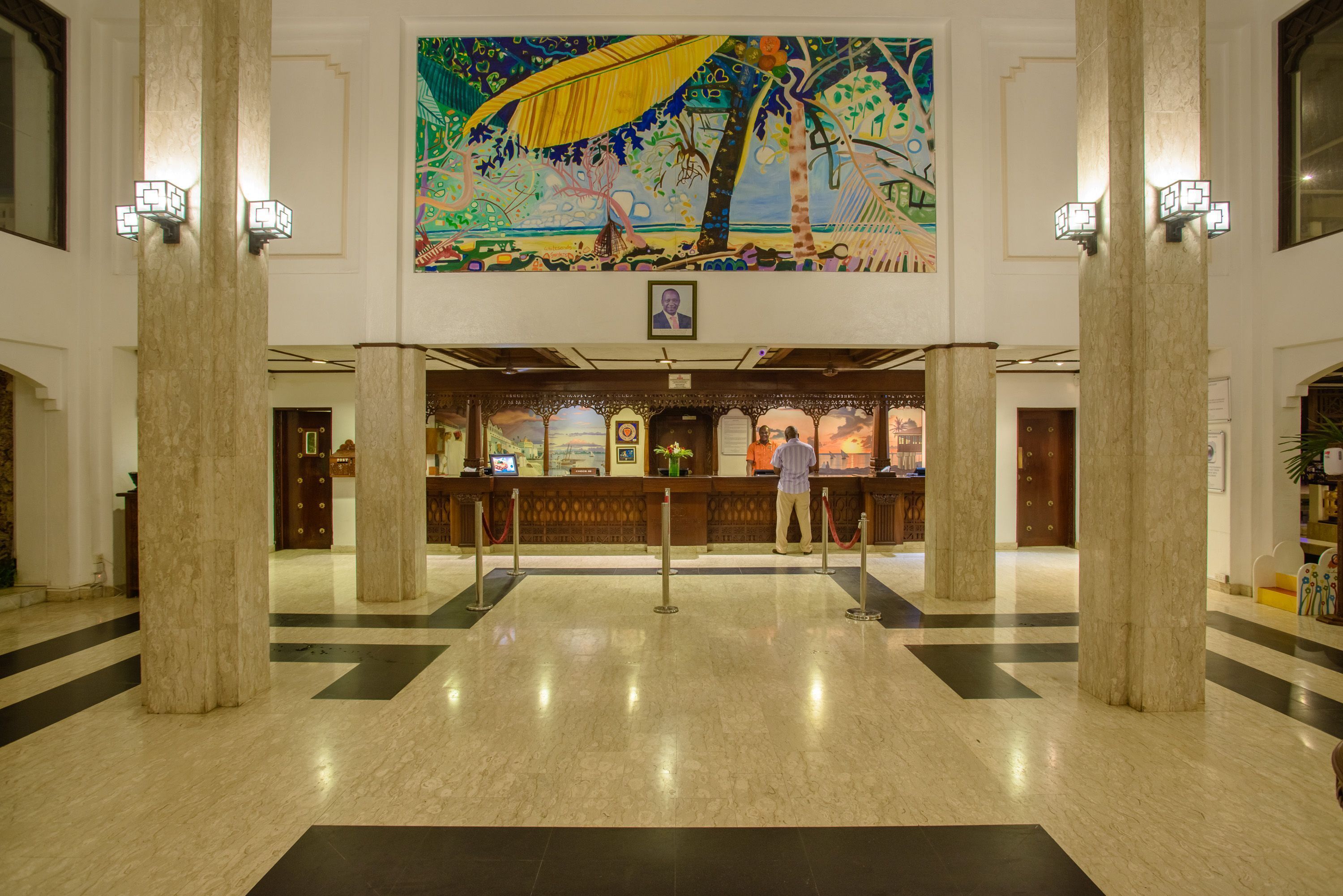 Un hall d’entrée avec un sol en marbre, un comptoir de réception et une grande fresque murale au-dessus.