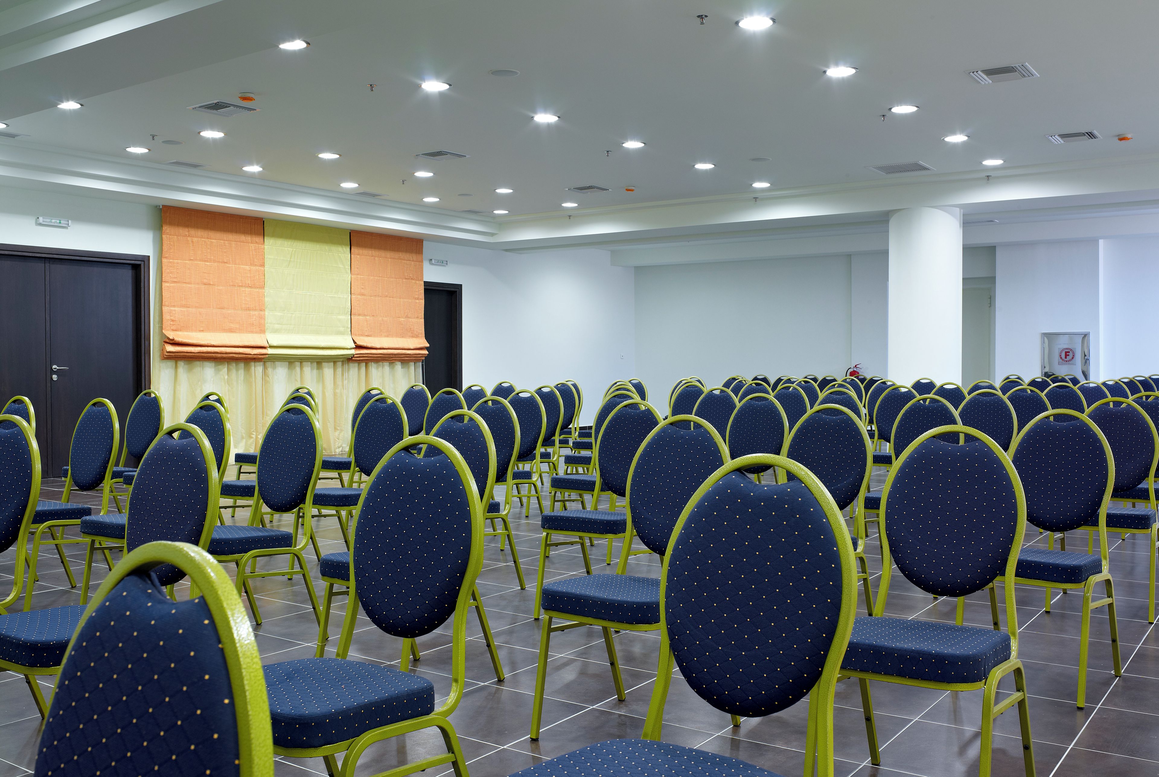 A conference room with rows of chairs, a stage, and a door.