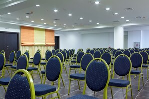 A conference room with rows of chairs, a stage, and a door. - Filion Suites Resort & Spa (Mylopotamos)