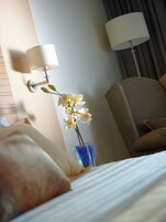 Una habitación de hotel con una cama, una mesita de noche con lámpara, un jarrón con flores y una silla.