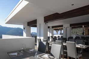 An outdoor dining area with tables and chairs, overlooking a mountainous landscape. - Filion Suites Resort & Spa (Mylopotamos)