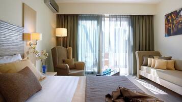 Habitación de hotel con una cama grande, dos sillones, un sofá, un escritorio y un ventanal con cortinas.