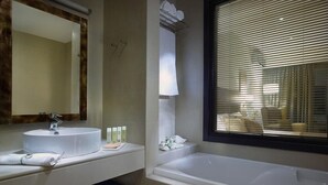 A modern bathroom with a sink, mirror, and bathtub. There are towels and toiletries on the counter. - Filion Suites Resort & Spa (Mylopotamos)