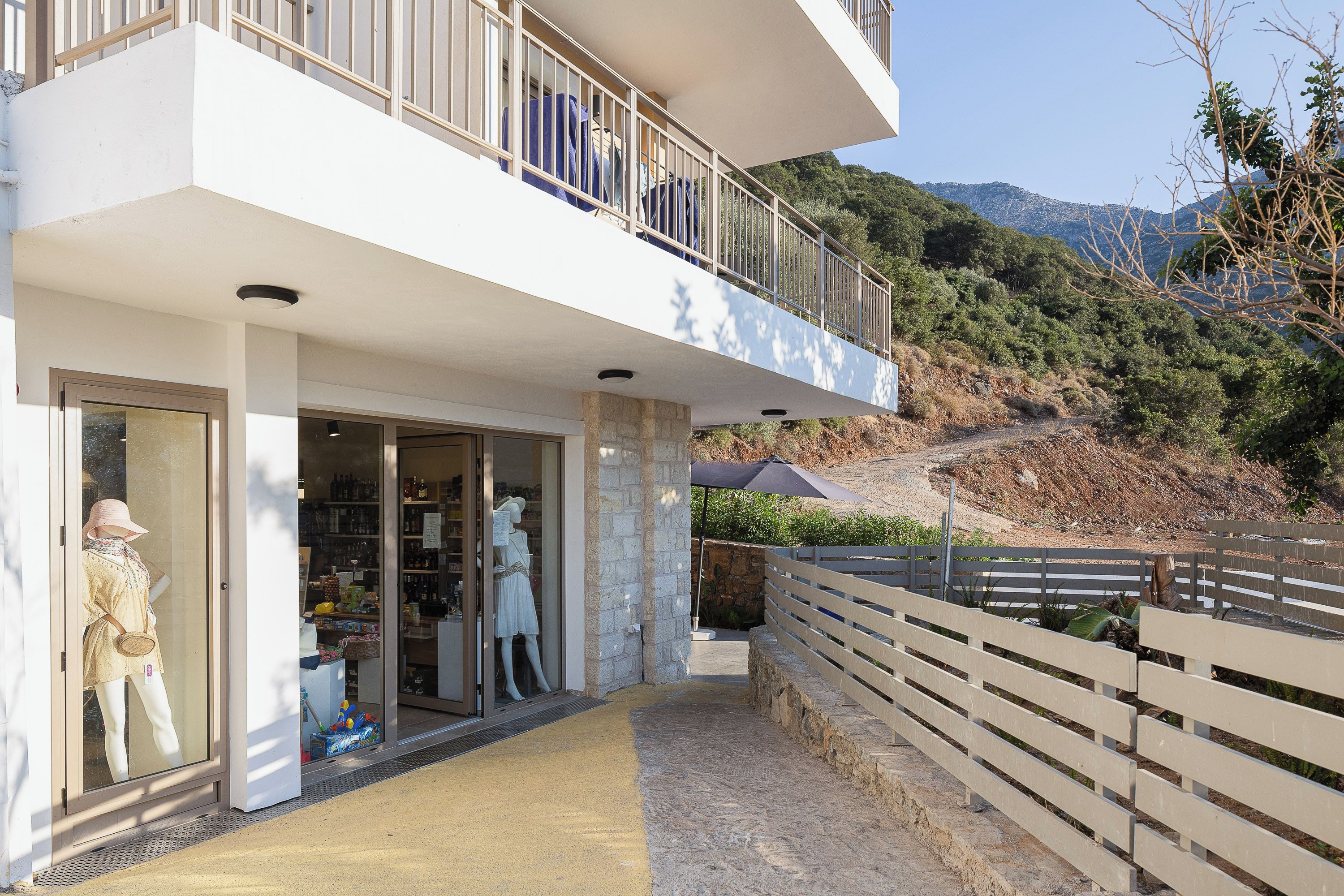 A two-story building with a balcony, a shop entrance, and a view of a hilly landscape.