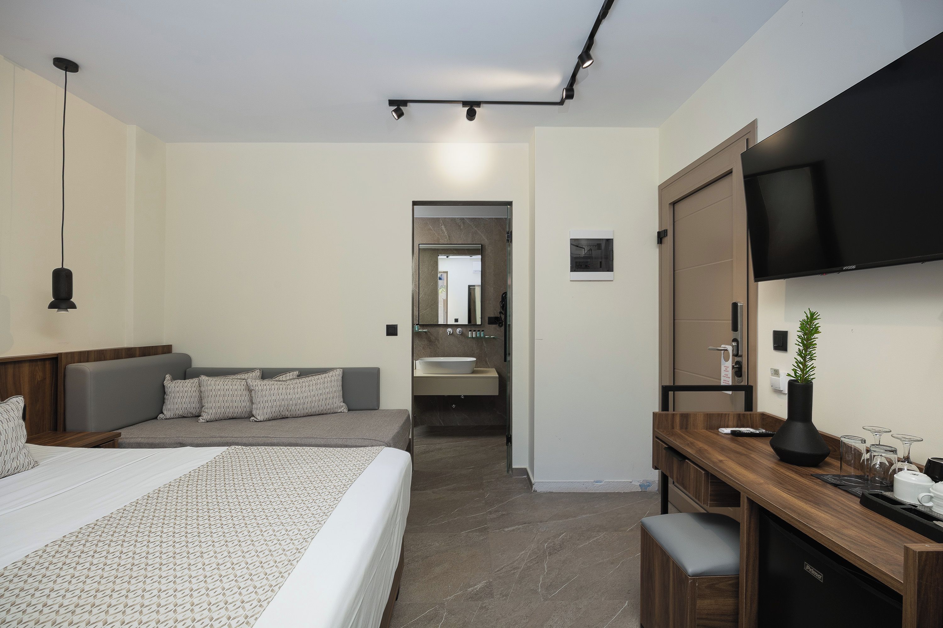 Ein modernes Hotelzimmer mit einem großen Bett, einem Schreibtisch, einem Fernseher und einem durch eine geöffnete Tür einsehbaren Badezimmer.