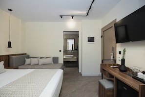 A modern hotel room with a large bed, a desk, a TV, and a bathroom visible through an open door.