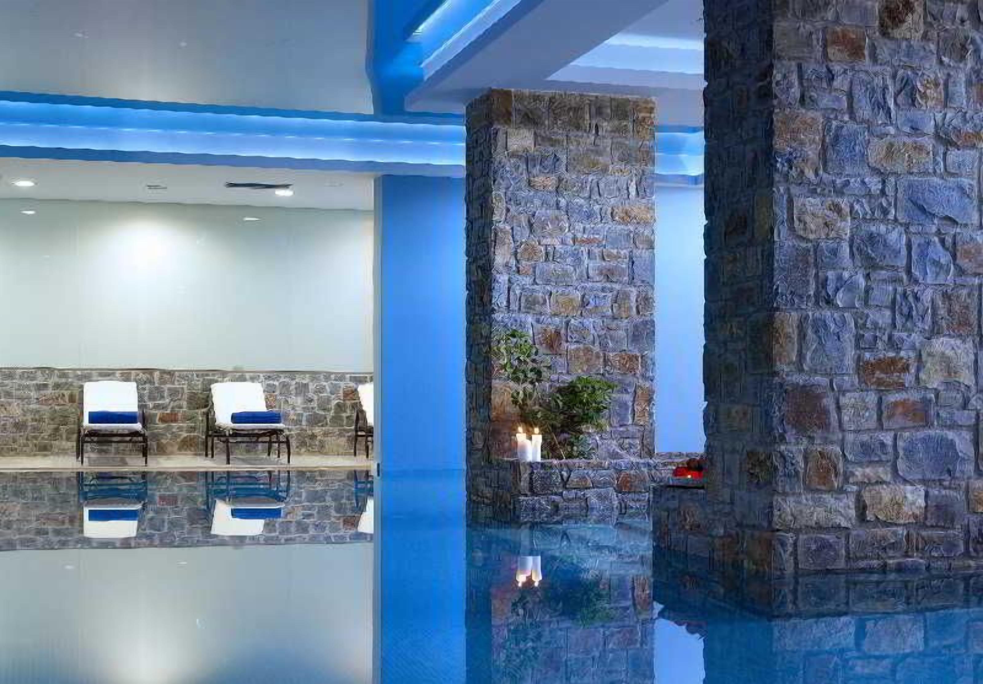 Zona de piscina con pilares de piedra, sillas de descanso y una piscina cristalina.
