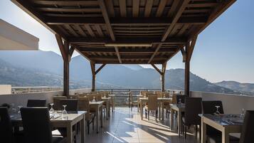 Un patio al aire libre con mesas y sillas, una pérgola de madera y vistas a montañas distantes.