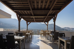 An outdoor patio with tables and chairs, a wooden pergola, and a view of distant mountains. - Filion Suites Resort & Spa (Mylopotamos)