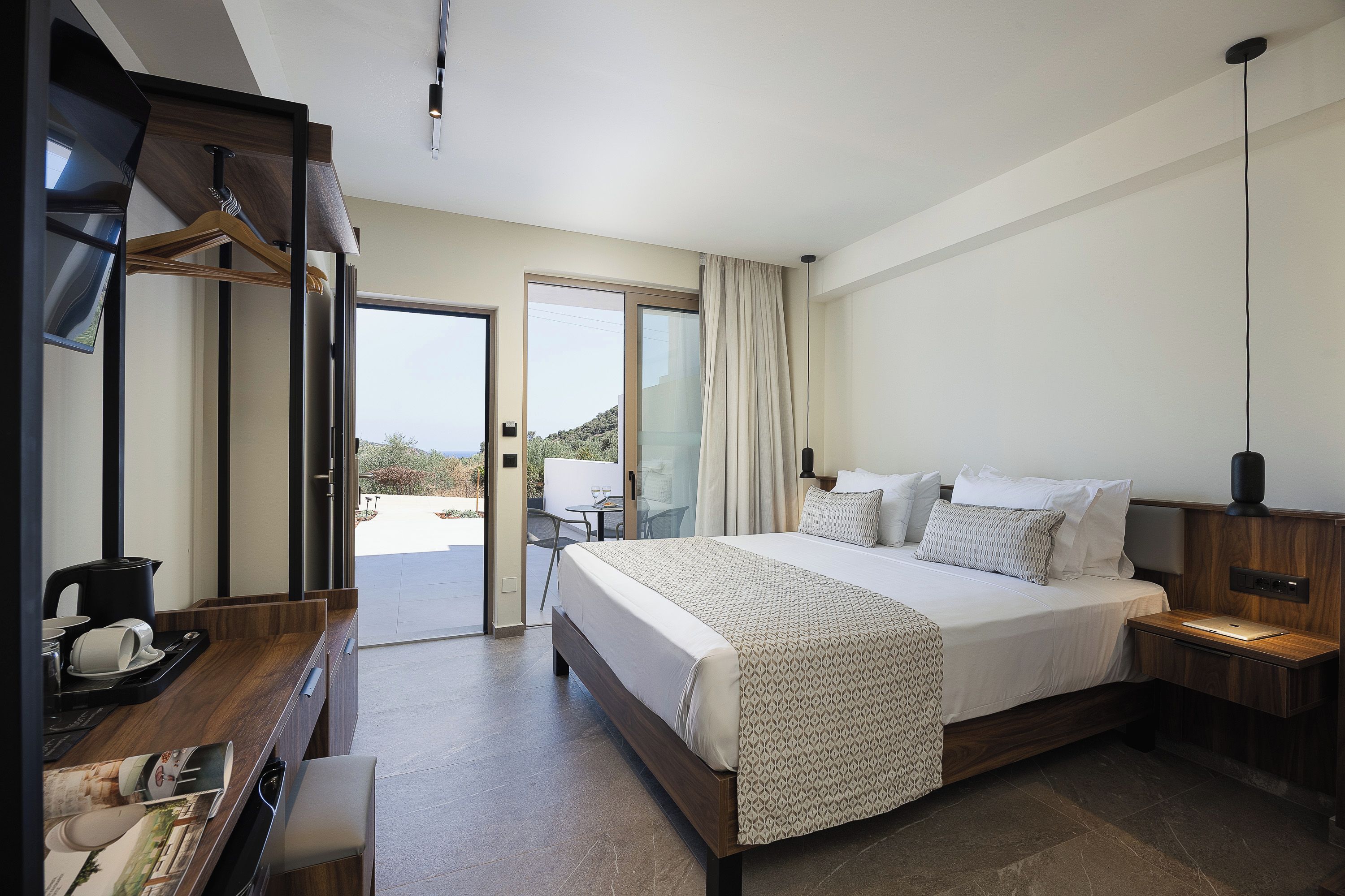 Habitación de hotel con cama, mesita de noche y escritorio con hervidor.