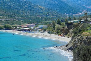 Una playa costera con aguas azules cristalinas, una orilla arenosa y colinas al fondo.