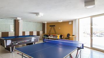 A pool table, a foosball table, and a ping pong table in a room with a large window.