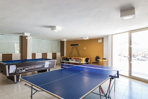 A pool table, a foosball table, and a ping pong table in a room with a large window. - Filion Suites Resort & Spa (Mylopotamos)