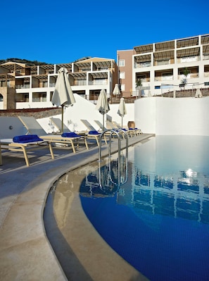 A swimming pool with sun loungers and umbrellas, surrounded by a building with balconies. - Filion Suites Resort & Spa (Mylopotamos)