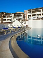 Una piscina con tumbonas y sombrillas, rodeada por un edificio con balcones.