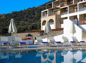 A poolside area with lounge chairs and umbrellas, a stone wall, and a building with balconies. - Filion Suites Resort & Spa (Mylopotamos)