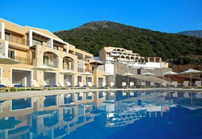 Ένα ξενοδοχείο με πισίνα, εξωτερικό χώρο για καθιστικό και ένα εντυπωσιακό ορεινό τοπίο στο βάθος.